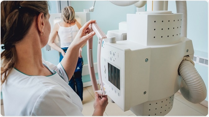 Radiologist and patient in a x-ray room. Classic ceiling-mounted x-ray system. Image Credit: Romaset / Shutterstock