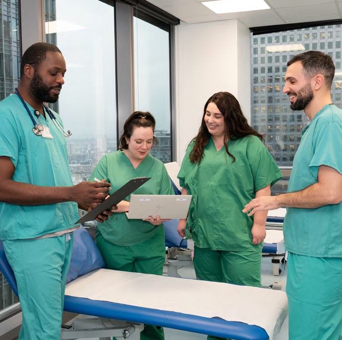 Four doctors in green scrubs stand in a semicircle, smiling at a clipboard. The image presents how the team works well together.