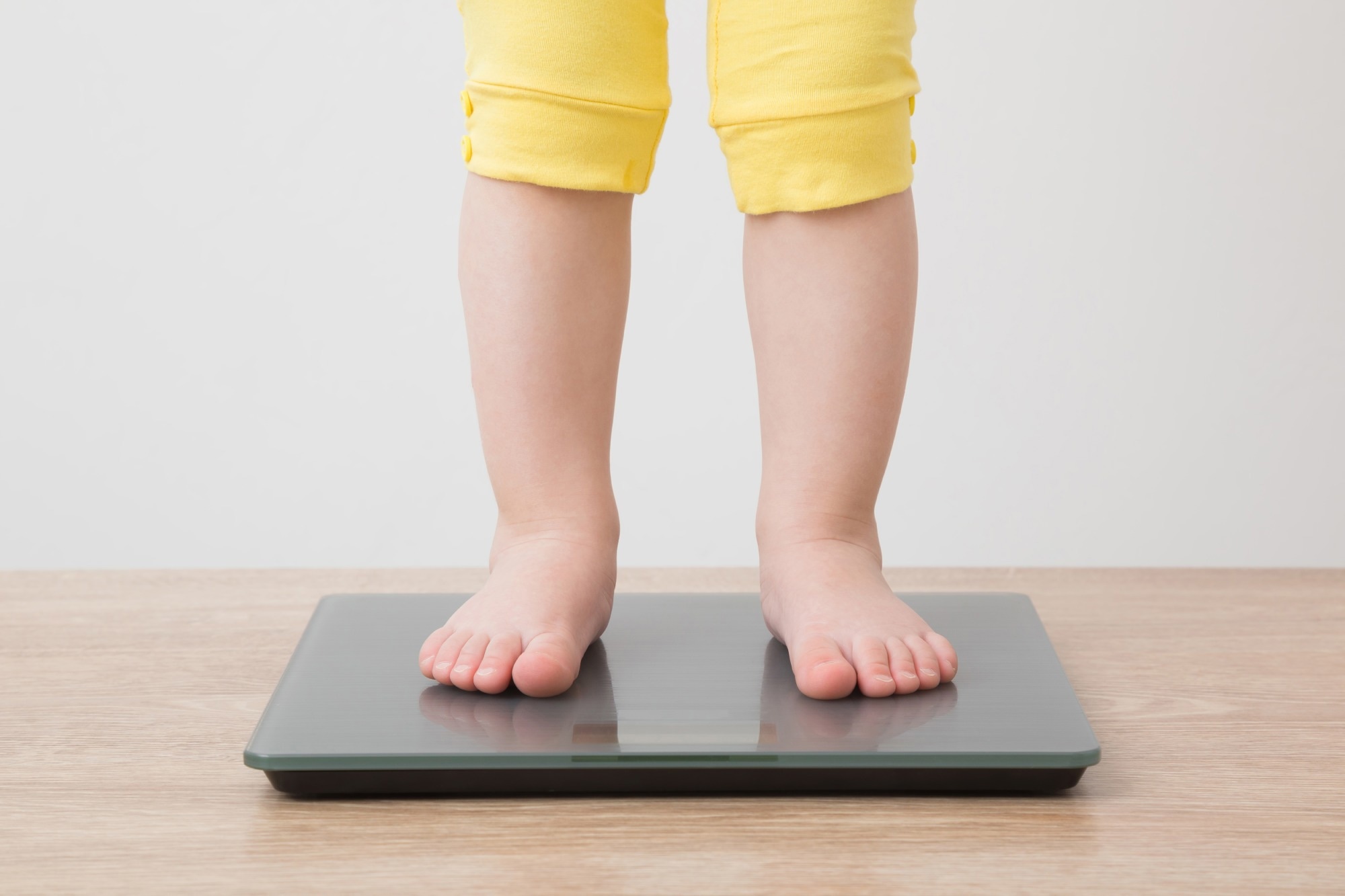 Baby girl with barefoot standing on weight scales