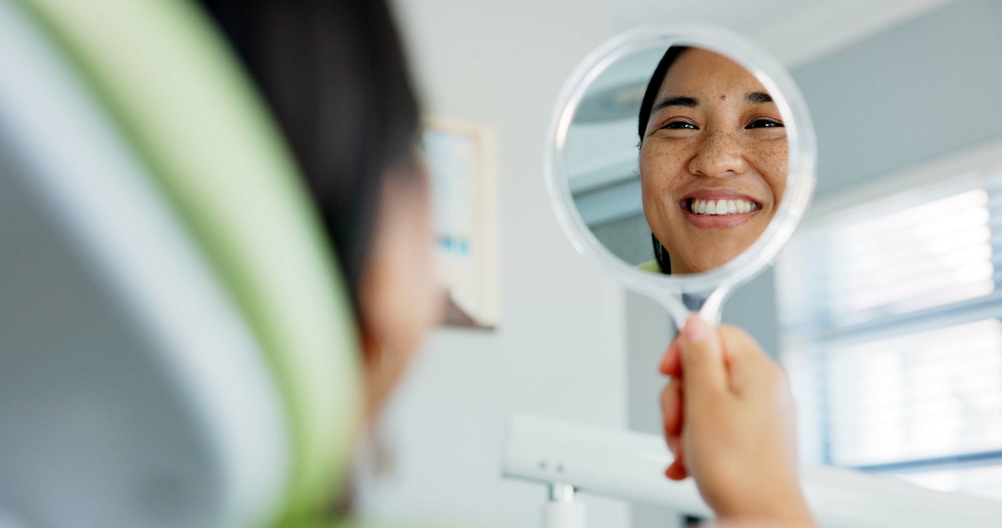 Happy woman with mirror check at a dentist for teeth whitening results