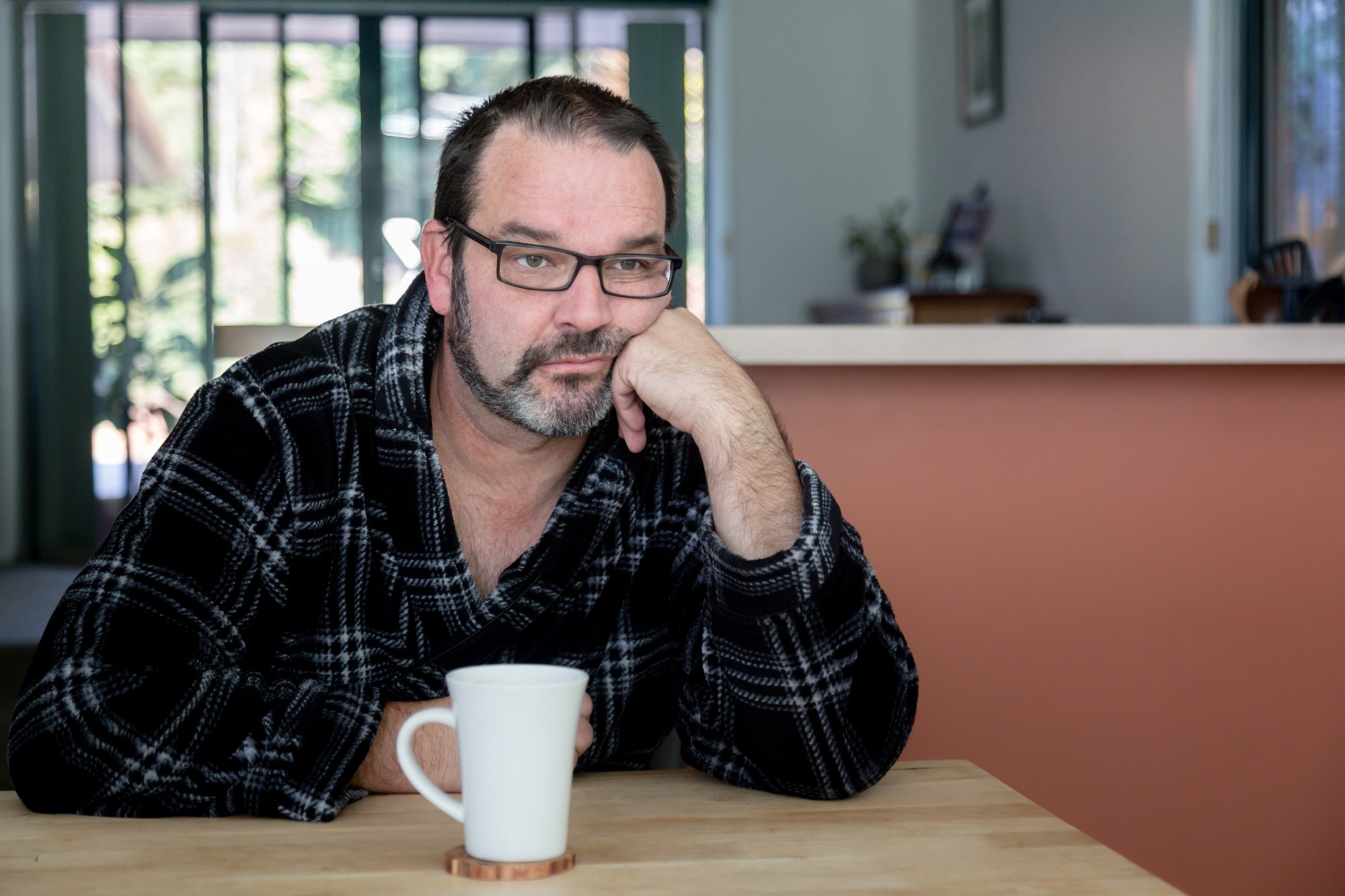 Middle aged man sitting at dining room table with coffee mug looking sad and depressed