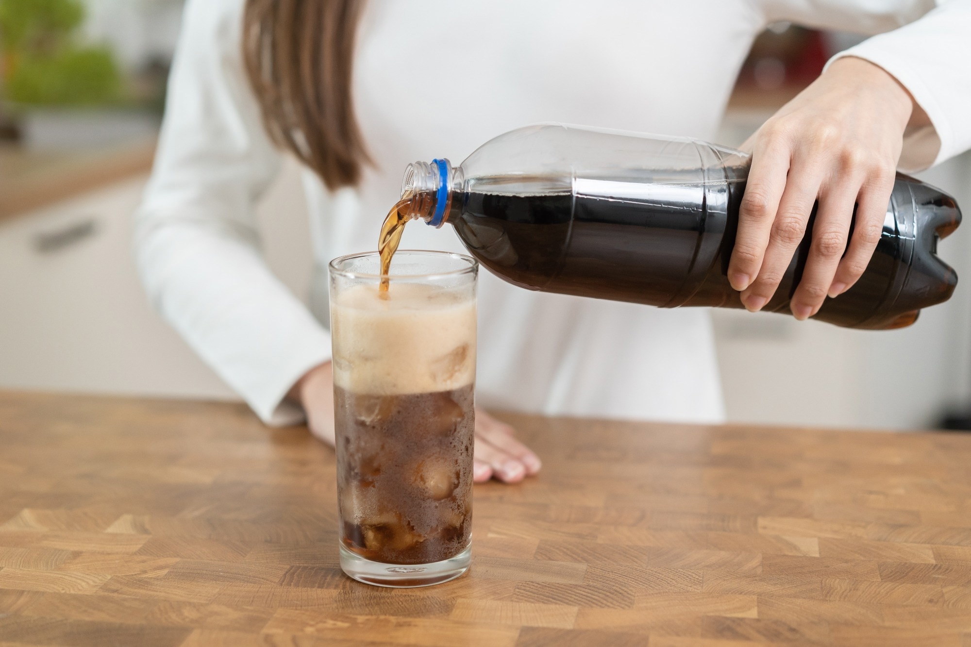 woman pouring fizzy cola soda into a glass of ice
