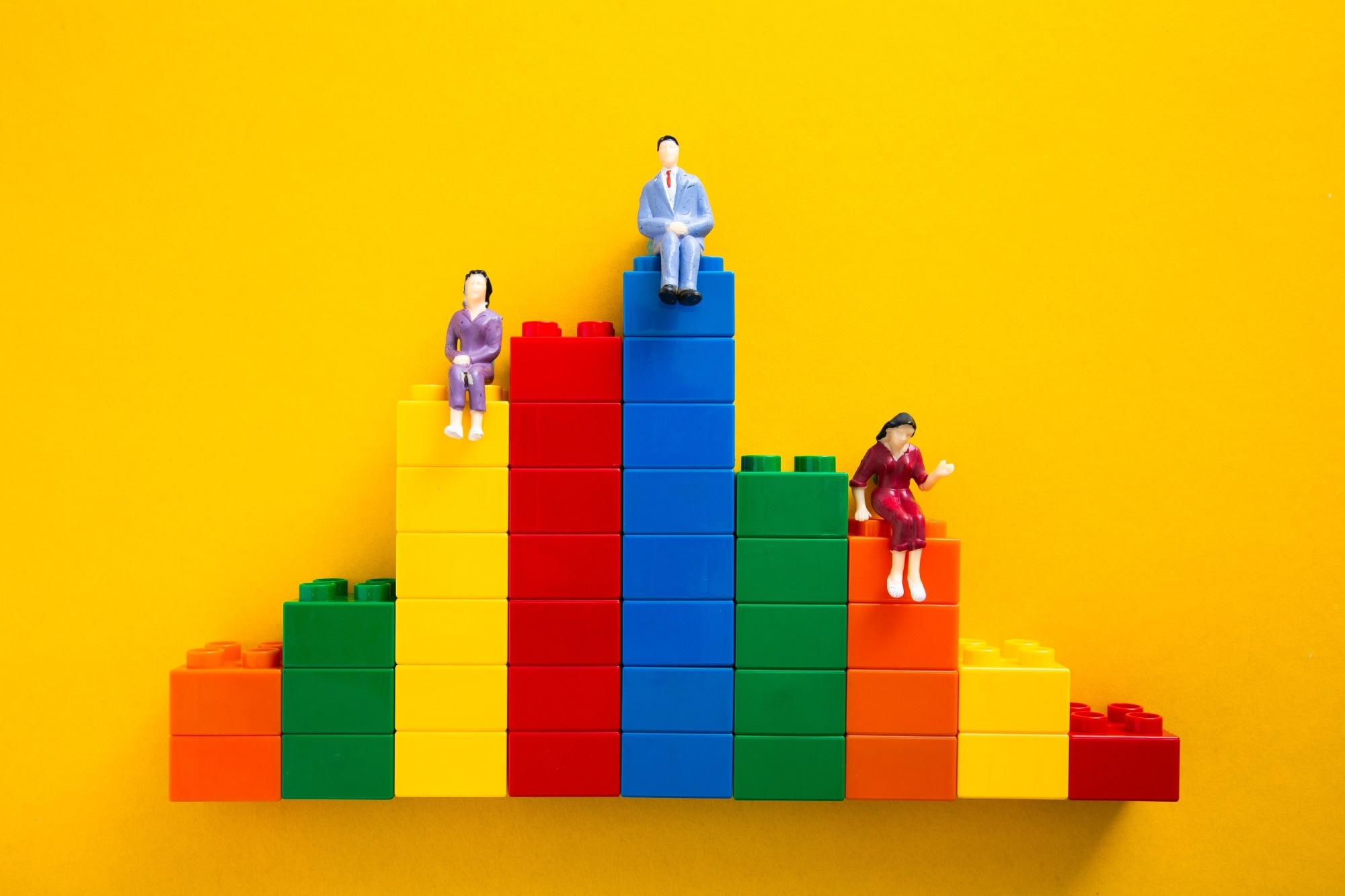 Concept of inequality: plastic figures sat on Lego blocks of different heights