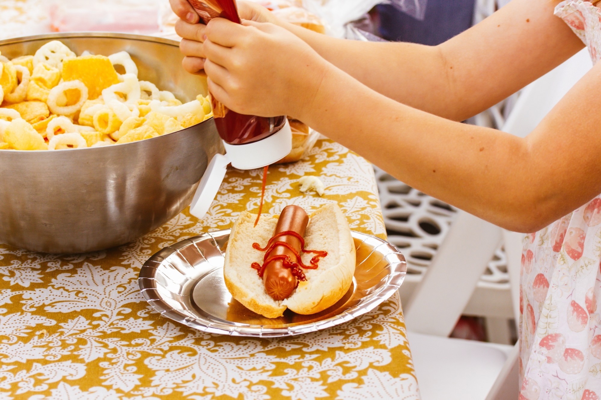 A little girl squeezing ketchup on a hotdog