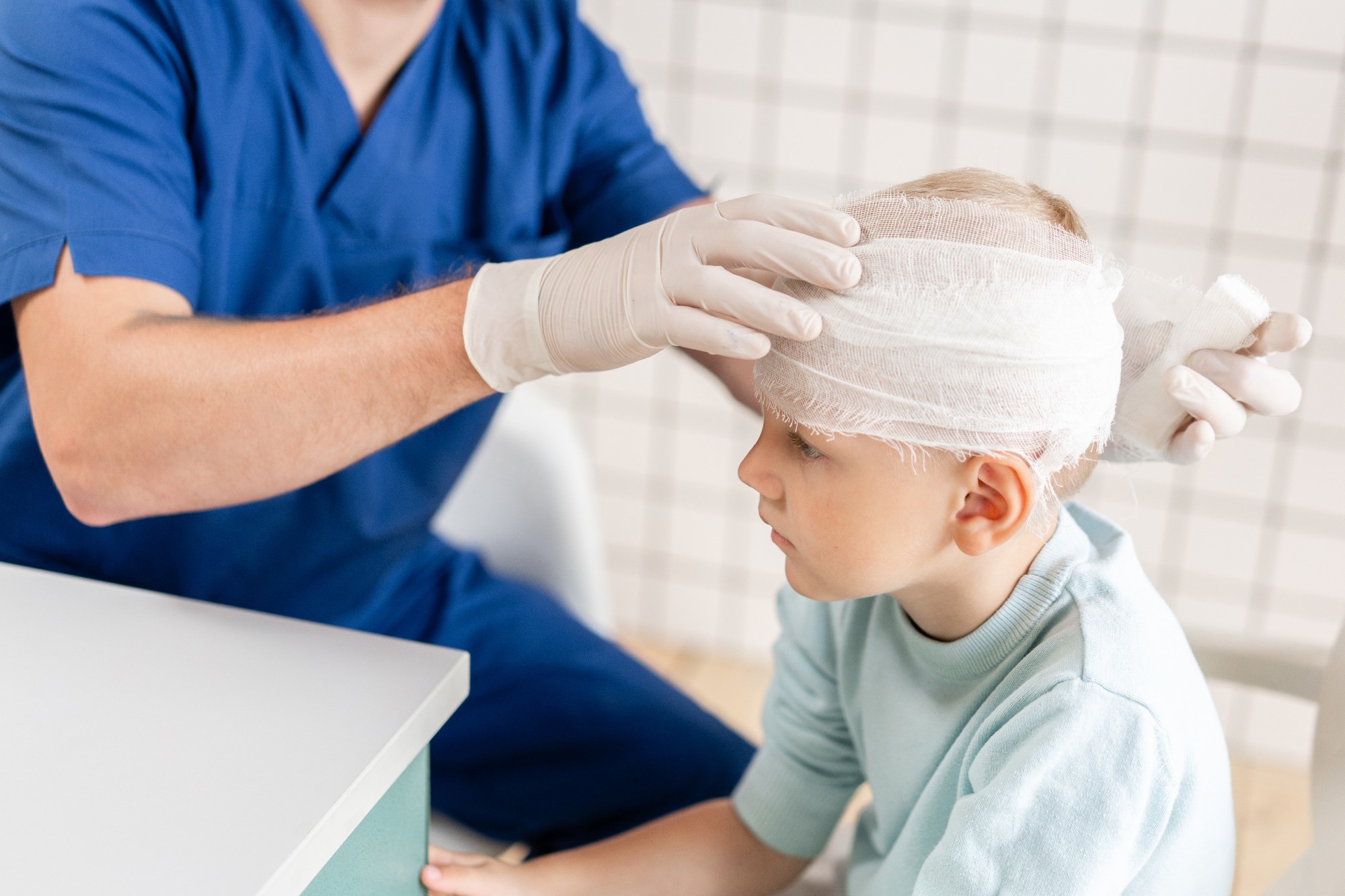 Doctor in blue scrubs wrapping a bandage around a young boys head