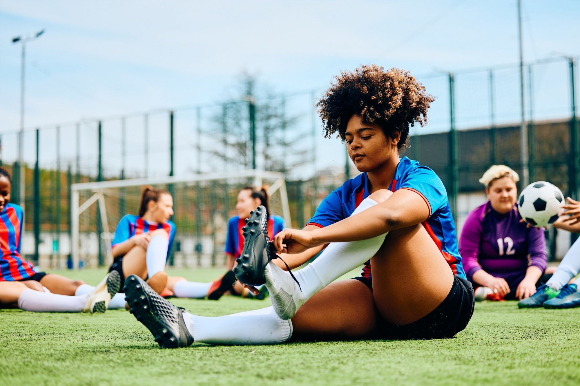 Young female footballer sat on pitch putting on training shoes