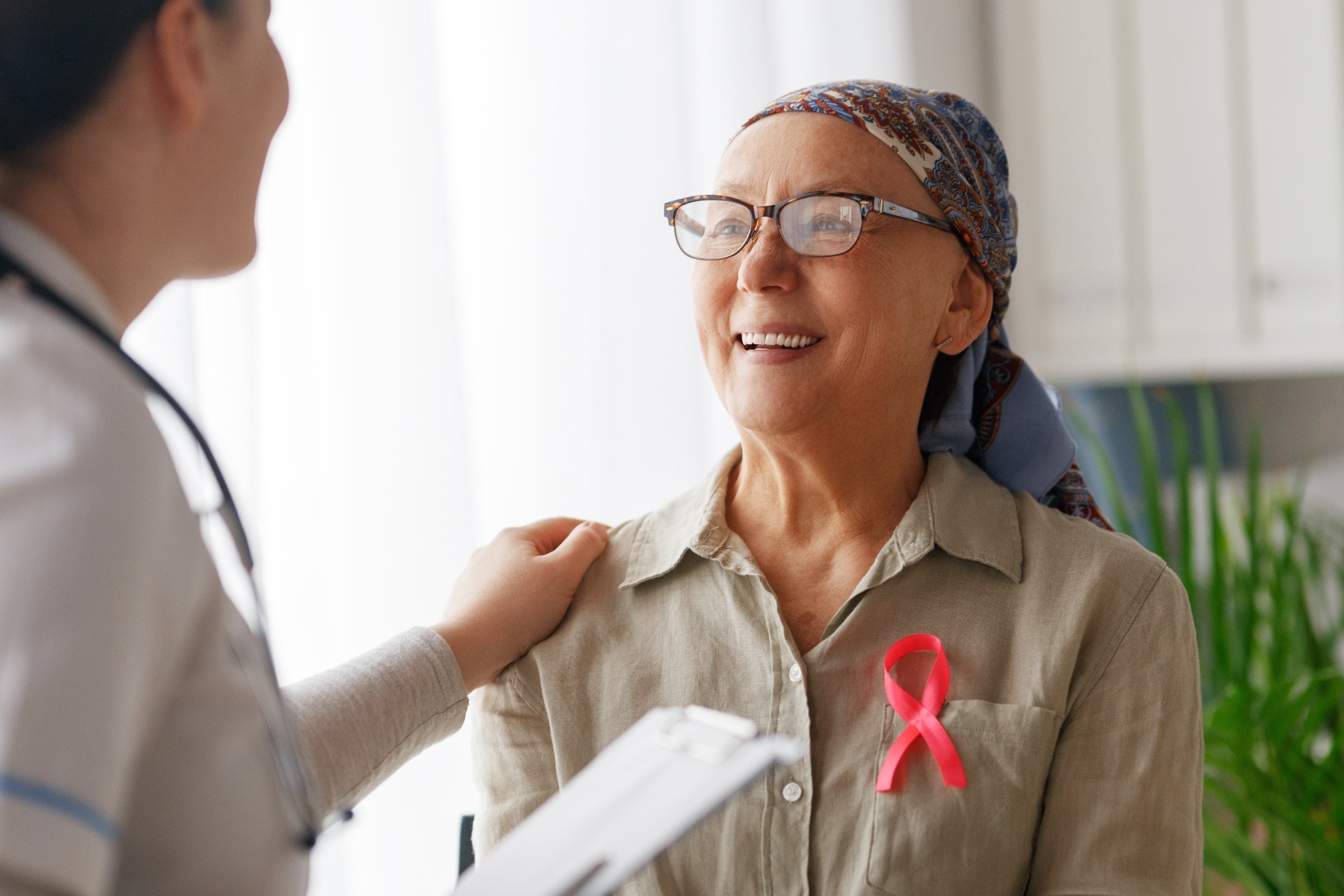 Female cancer patient wearing scarf on her head and a pink breast cancer ribbon talking to friendly medical staff